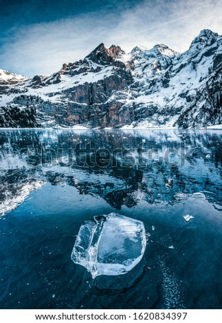 beaufiful clear chunk of ice on frozen lake Oeschinensee with reflection and Blümlisalp Mountains in Berner Oberland Royalty-Free Stock Photo #1620834397