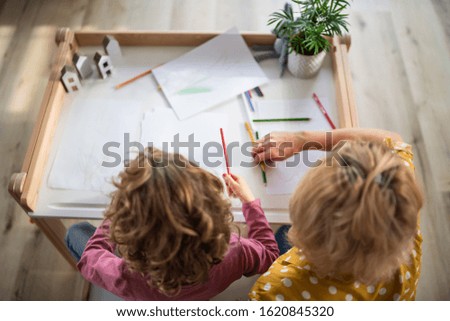 A top view of small girl with mother indoors at home, drawing pictures.