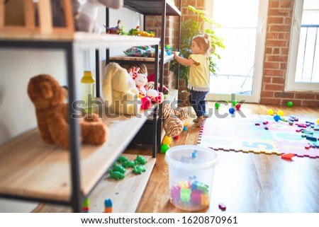 Beautiful toddler standing taking toys of shelving at kindergarten