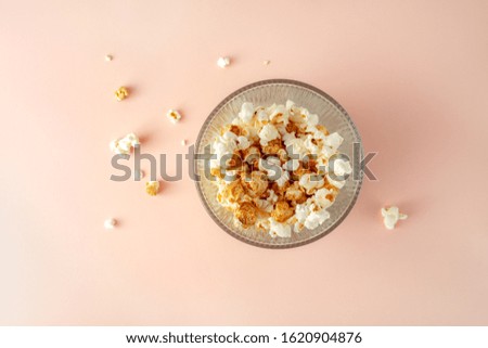 Popcorn in a glass bucket on pink colored background, top view, horizontal orientation