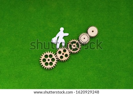 Silhouette of a man climbing up wooden gears on a green background. The concept of business, promotion.