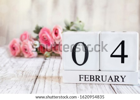 White wood calendar blocks with the date February 4th. Selective focus with pink ranunculus in the background over a wooden table. 
