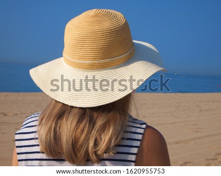 
A young girl in a hat is resting on the sea beach. Back view.