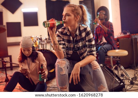 Multi-ethnic group of young people in music studio focus on pretty young woman drinking beet in foreground