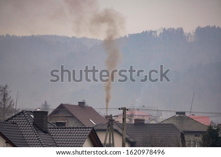 black smoke comes from chimney of a house against gray sky, heating with coal in winter. environmental problem of smog in Beskid Mountains, Zywiec, Krakow. heating system needs to be Royalty-Free Stock Photo #1620978496