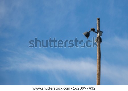 Two baseball field lights on an old telephone pole, isolated against blue sky with wispy clouds.  Daytime shot where the lights are not on.  