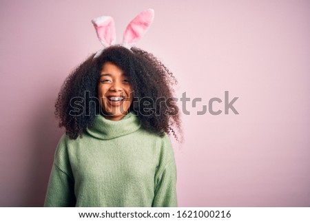 Young african american woman with afro hair wearing easter rabbit ears costume over pink background with a happy and cool smile on face. Lucky person.