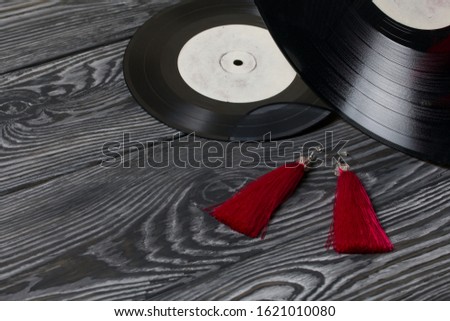 Homemade tassel earrings in red. Against the background of old vinyl records and brushed pine boards painted in black and white.