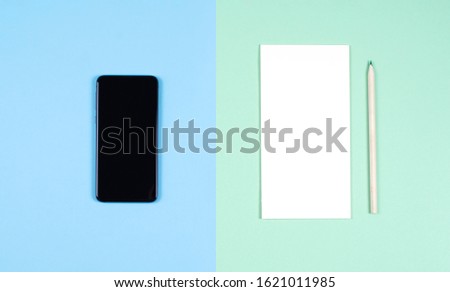 A modern smartphone and a paper notebook with a pencil. The concept of digital detox. Blue and green background