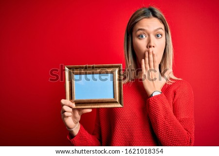 Young beautiful woman holding vintage frame standing over isolated red background cover mouth with hand shocked with shame for mistake, expression of fear, scared in silence, secret concept