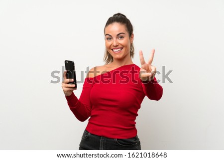 Young woman using mobile phone smiling and showing victory sign