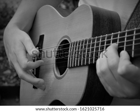 Acoustic guitar being played showing strings fret board guitar and hands in black and white