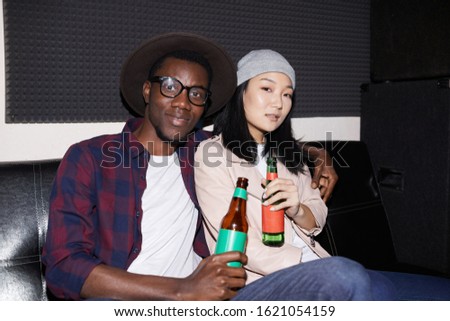 Portrait of modern young couple posing with beer bottles while enjoying nightclub party, shot with flash