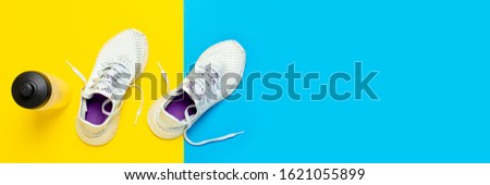 White running shoes and a water bottle on an abstract yellow and blue background. Concept of running, training, sport. Banner. Flat lay, top view