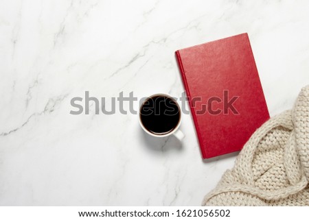 Cup with coffee or tea, a knitted scarf and a book on a marble table. Concept of breakfast, education, knowledge, reading books, winter leisure. Flat lay, top view