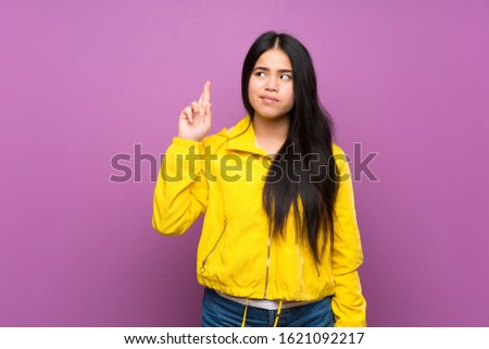 Young teenager Asian girl over isolated purple background with fingers crossing and wishing the best