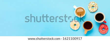 Tasty donuts and cups with hot drinks, coffee, cappuccino, tea on a blue background. Concept of sweets, bakery, pastries, coffee shop, meeting, friends, friendly team. Banner. Flat lay, top view