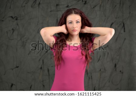 Glamorous Model is smiling and talking cute to the camera. Portrait of a pretty slim brunette woman with emotions in a pink dress and with brown hair on a gray background in the studio.