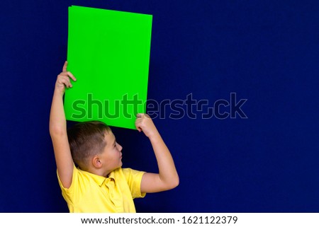 Side view  Caucasian schoolboy posing with blank paper against blue background.