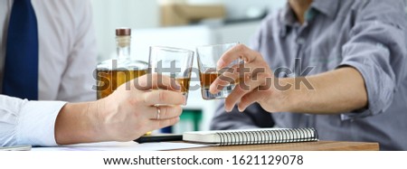 Close-up of hands businessmen holding glasses with alcohol drinks. Partners celebrating signing profitable contract in office. Business negotiations concept