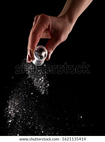 Female hand with red manicure pours glitter on black background