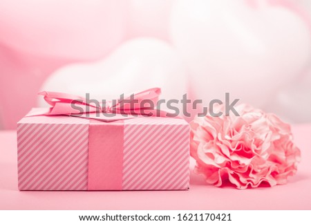 Valentine Day gift in a box wrapped in striped paper and tied with silk ribbon bow and heart shaped greeting card and rose flower on pink background with copy space for text