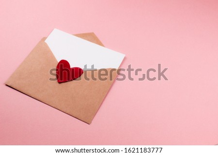 Love letter with white paper sheet in craft paper envelope with red heart flat lay on colorful pink background. 8 march, Mother's day, Valentine's Day template. Top view with copy space. Stock photo