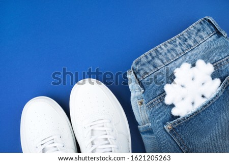Flatlay with white sneakers and jeans with a snowflake in the pocket isolated on blue background.