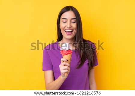 Young brunette woman with a cornet ice cream over isolated yellow background