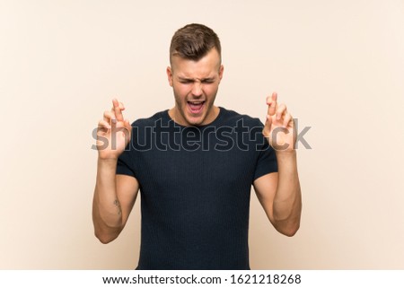 Young handsome blonde man over isolated background with fingers crossing