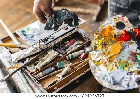 Young male painter at art studio indoors holding palette and textile working process close-up