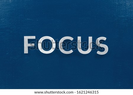 the word focus laid with silver metal characters on blue painted wooden board in flat lay with central composition.