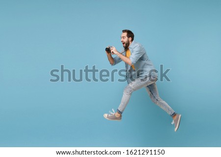 Cheerful traveler tourist man in yellow casual clothes with photo camera isolated on blue background. Male passenger traveling abroad on weekend. Air flight journey concept. Jumping, taking pictures
