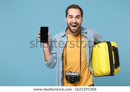 Excited traveler tourist man in casual clothes with photo camera isolated on blue background. Passenger traveling abroad on weekends. Air flight journey. Hold suitcase, mobile phone with empty screen