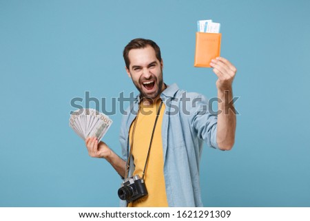 Happy traveler tourist man in yellow clothes with photo camera isolated on blue background. Passenger traveling on weekends. Air flight journey. Hold passport boarding pass tickets fan of cash money
