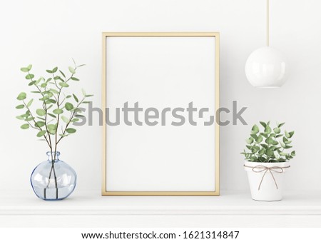 Interior poster mockup with vertical gold metal frame on the table with plants in blue vase and hanging lighting on empty white wall background. A4, A3 size format. 3D rendering, illustration.