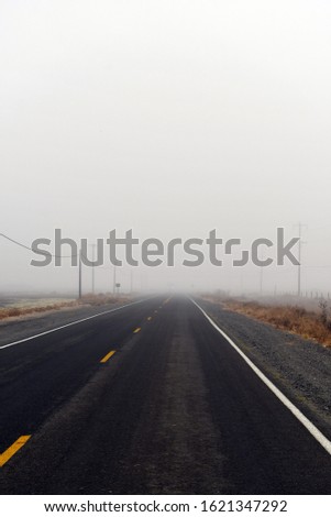 Road with white and yellow dashed lines in it with fog