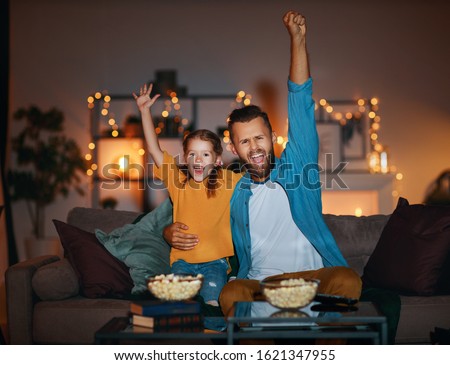 family   father and child daughter watching projector, TV, movies with popcorn in the evening   at home 
