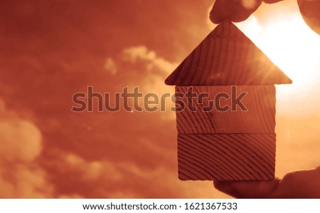hand holds the last pieces of wooden house puzzle on blue sunny sky background. wooden home made from natural material of jigsaw. puzzle in the form of wood house. for sale or rent.