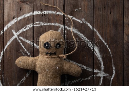 Voodoo doll on a wooden background with dramatic lighting. The concept of witchcraft and black art and the occult. Burlap doll on the background of a drawn star. Copy space.