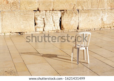 An empty chair at the Kotel Wailing Western Wall, a remnant of the ancient wall that surrounded the Jewish Temple's the most sacred site recognized by the Jewish faith outside of the Temple Mountain.  Royalty-Free Stock Photo #1621431499