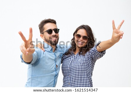 Happy couple in sunglasses showing victory sign. Front view of beautiful cheerful young couple in sunglasses posing together. Happiness concept
