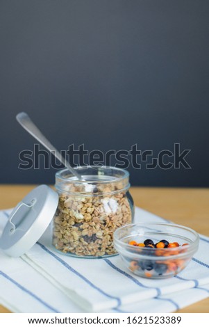 baked muesli with nuts and oat flakes, sea buckthorn and blueberry berries in glass bowl on striped textile napkin on wooden table, close up view from above of vertical still life stock photo image