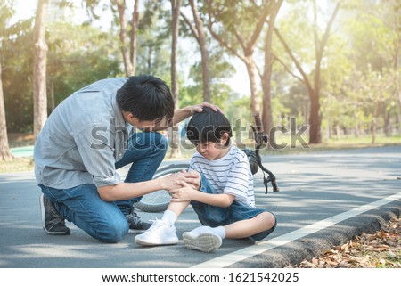 Young asian father of dad calms son that fell from the bike and he get injury on knee and leg while have weekend leisure in public park,accident can happen everywhere and every time. Royalty-Free Stock Photo #1621542025