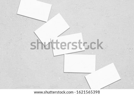 Close up of empty white rectangle business card mockups lying diagonally with soft shadows on neutral light grey concrete background. Flat lay, top view. Open composition.