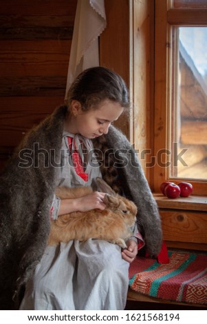 girl in a traditional Russian dress with a rabbit in her arms on a rustic background, long braids, Easter
