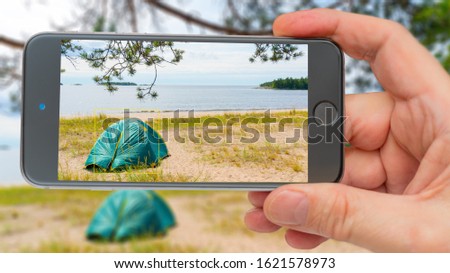 Tents on sandy shore of lake. Photo smartphone. Smartphone in hand. Tourist tent on screen.