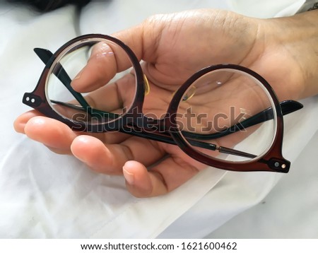 Woman's hand holding   shortsighted or nearsighted eyeglasses on white pillow, white bed background, Close up & Macro shot, Selective focus, Optical concept Royalty-Free Stock Photo #1621600462