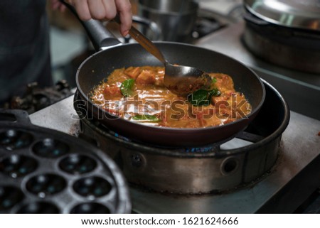 A picture of a cook's hand preparing a Thai food menu in the kitchen using his hands to cook the pan. That has food in the container.