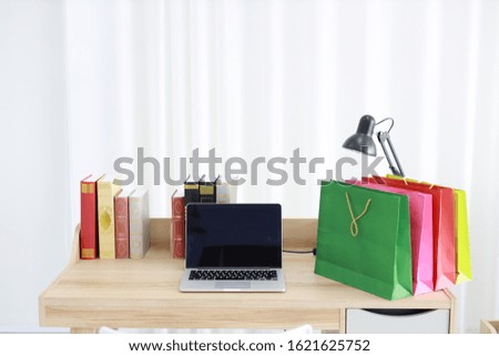 Computer black blank screen on wooden working table with books and shopping bags in room house indoor. Free space for your advertisement 